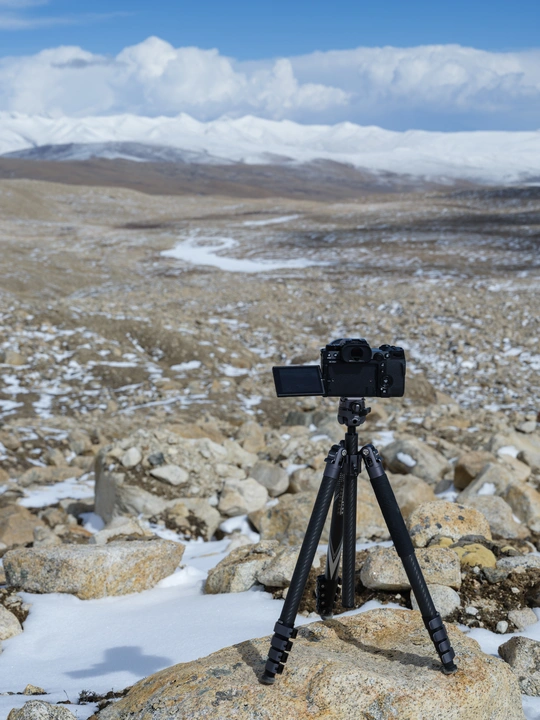tripod 上的一部相机正在拍摄有雪山的岩石景观照片