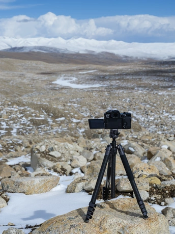 tripod 上的一部相机正在拍摄有雪山的岩石景观照片