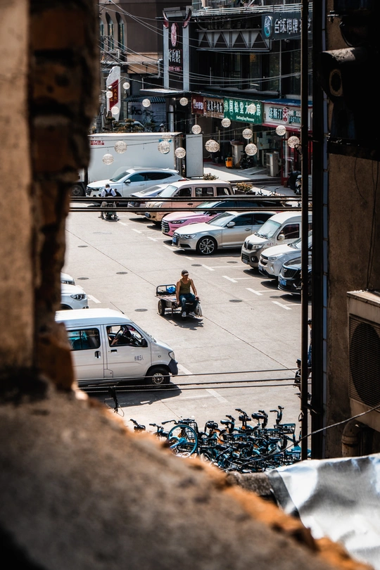 从停满汽车和摩托车手的停车场窗口看下去 摩托车在城市街道上行驶。