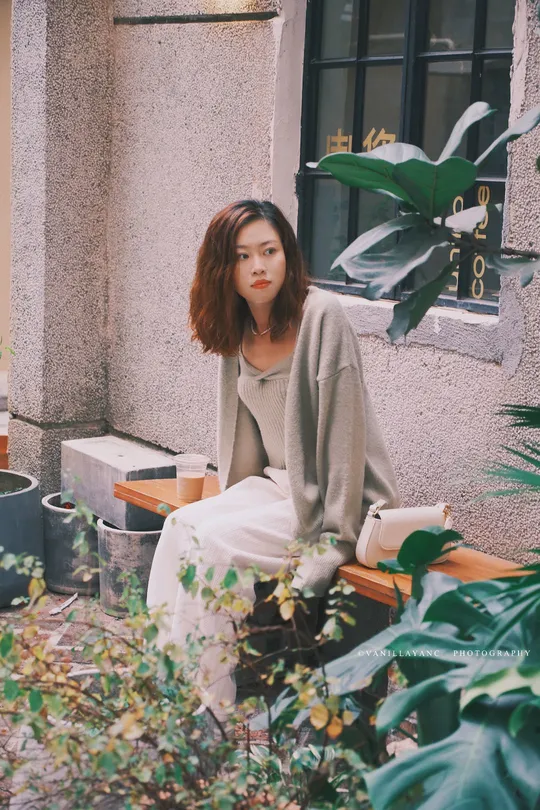 一个人坐在建筑物前的长凳上 周围有植物。