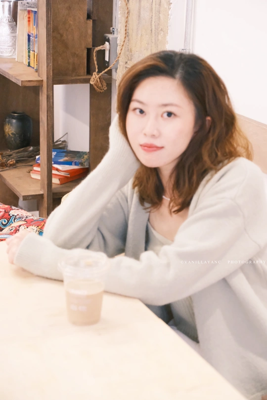 一个年轻女子坐在桌子旁 手中拿着一杯白色的咖啡。