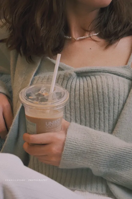 一位穿着毛衣拿着一杯咖啡的妇女 用吸管