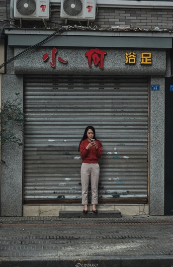 一位穿红衣服的女士站在街上的一栋建筑前