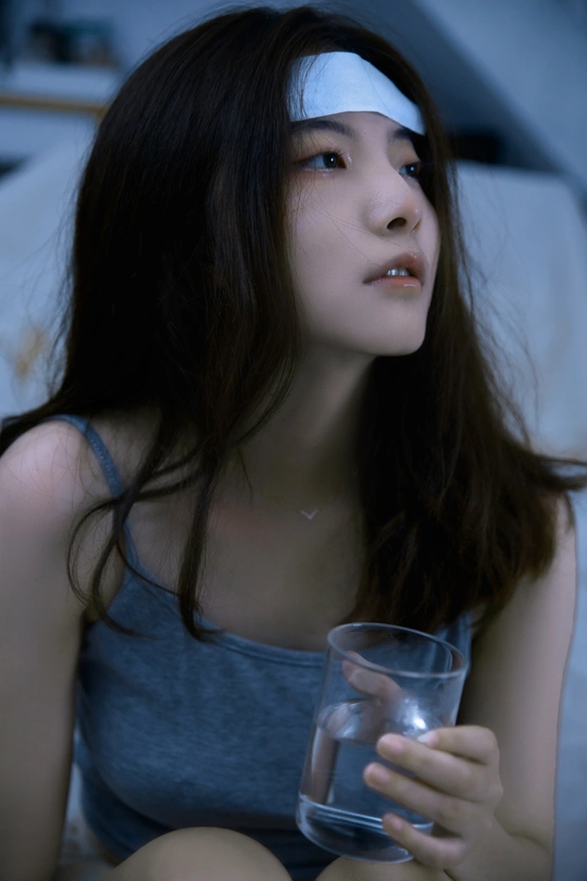 一个年轻女子坐在床上 手里拿着一杯水。