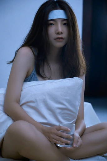 一个年轻女子坐在床上 地上放着一杯水。