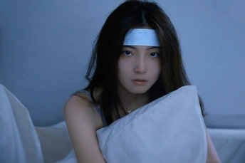 一个有蓝眼睛和额头上有绷带的女青年躺在床上 头下垫着枕头。