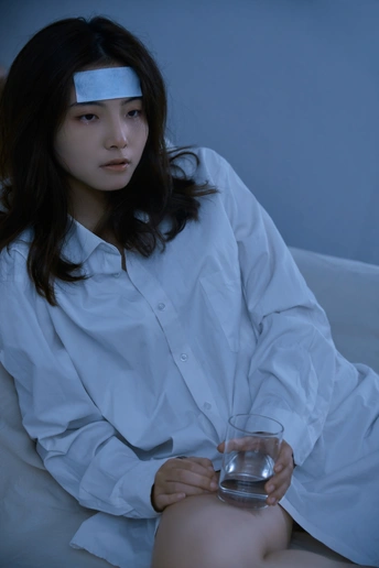 一个蓝眼睛的年轻女子穿着一件白衬衫坐在沙发上 手里拿着一杯水。