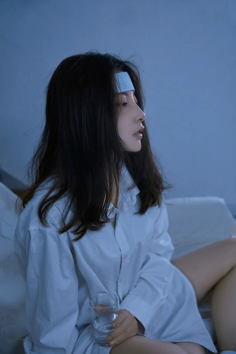 一个年轻女子坐在床上 面前放着一杯水。