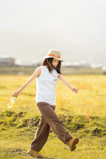 一位戴白色帽子 手持一瓶饮料 在草地上行走的年轻女子。