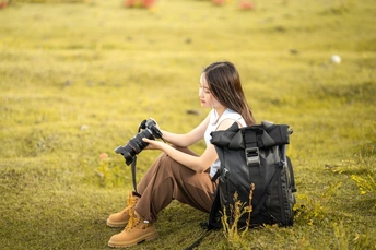 一个年轻女子坐在草地上 背着背包 拿着相机 正在拍照。