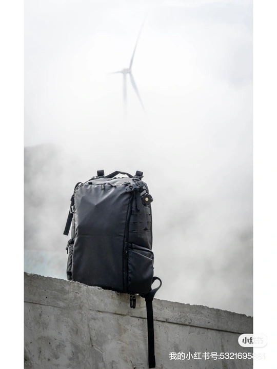 一个黑色手提箱或背包坐在混凝土墙的顶部 天空中有一架风车。