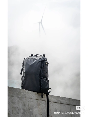 一个黑色手提箱或背包坐在混凝土墙的顶部 天空中有一架风车。