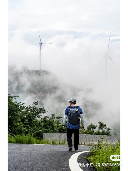 一位背包客沿着有风车背景的公路在雾中行走