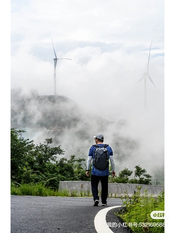 一位背包客沿着有风车背景的公路在雾中行走
