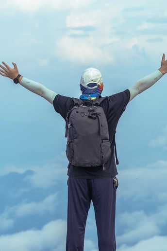一个背着背包的男子站在山顶 双手举过头顶 背景是白云和蓝天。
