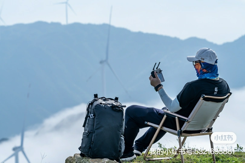一个坐在山顶椅子上的男人 背景是风车和山脉。