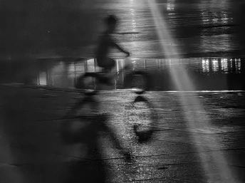 黑白色调 一个人在雨夜骑自行车 街上的人们打着伞走动。