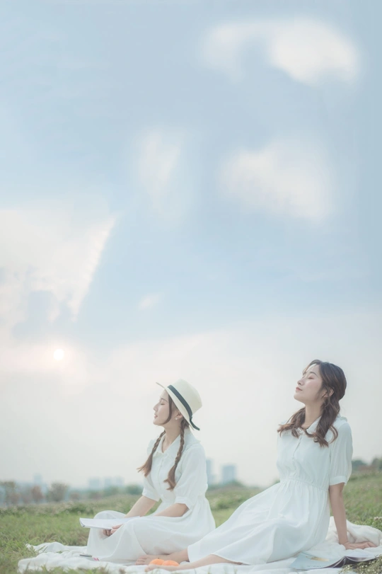 一个穿着白裙子的年轻女子坐在草地上 背景是天空中的一片云。