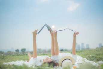 一个年轻女子躺在草地上 用毯子盖住自己 头枕在书上 在公园里阅读。