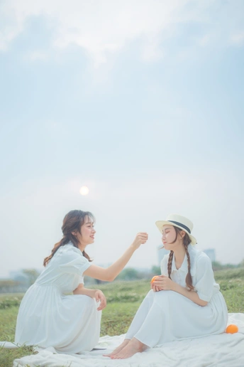 两个穿白色连衣裙的年轻女子坐在草地上的一块毛毯上