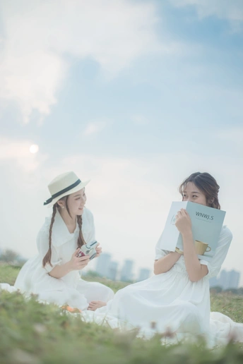 穿着白色衣服的年轻女性坐在草地上阅读书籍。