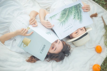 一个女性躺在草地上 正在阅读一本书 脸边放着一个棕榈叶盒子。