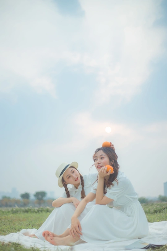 一个年轻女子和一个小女孩坐在草地上 手里拿着橙子。