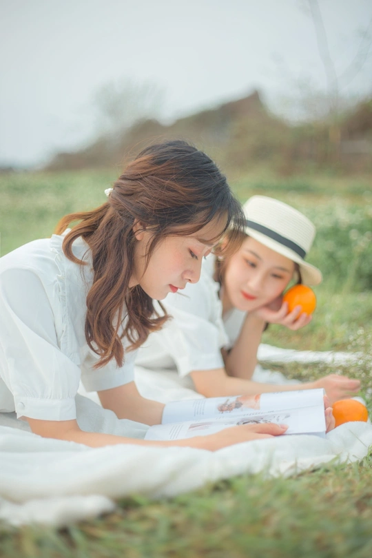 一个年轻女子正在给一个躺在草地上毯子上的小女孩读书。