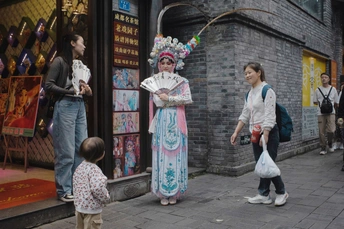 一位穿着服装的女人和一个小女孩站在人行道上 人们注视着她们。