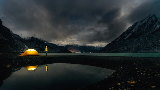 夜晚湖中映照着黄帐篷 背景是山脉。