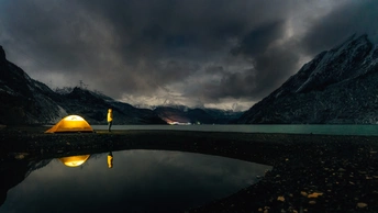 夜晚湖中映照着黄帐篷 背景是山脉。