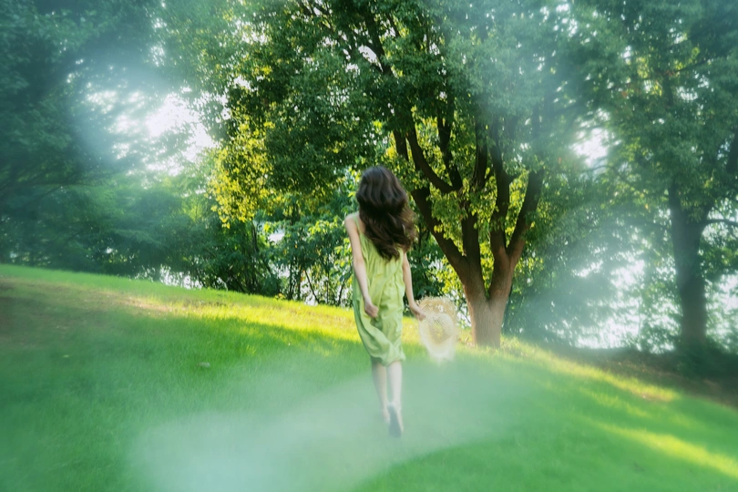 一位穿着绿色连衣裙的年轻女子穿越一片绿色的草地。