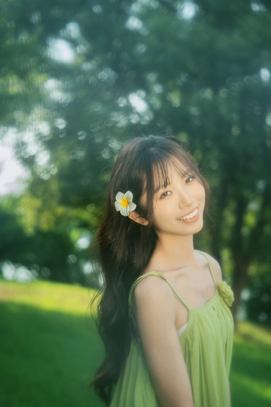 一位穿着绿色连衣裙的年轻女子站在公园里 头戴一朵花。