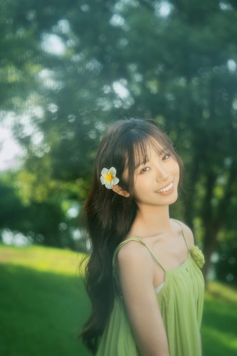 一位穿着绿色连衣裙的年轻女子站在公园里 头戴一朵花。