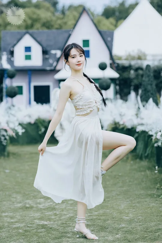 一位美丽的年轻女子穿着白色连衣裙在房子的院子里草坪上