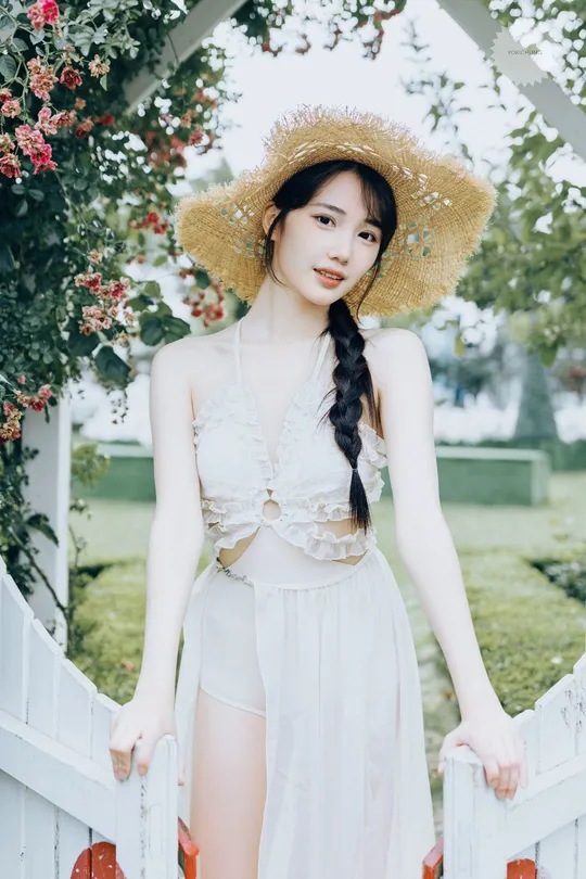 一位穿着长白色连衣裙和草编帽子的女人站在围栏旁边。