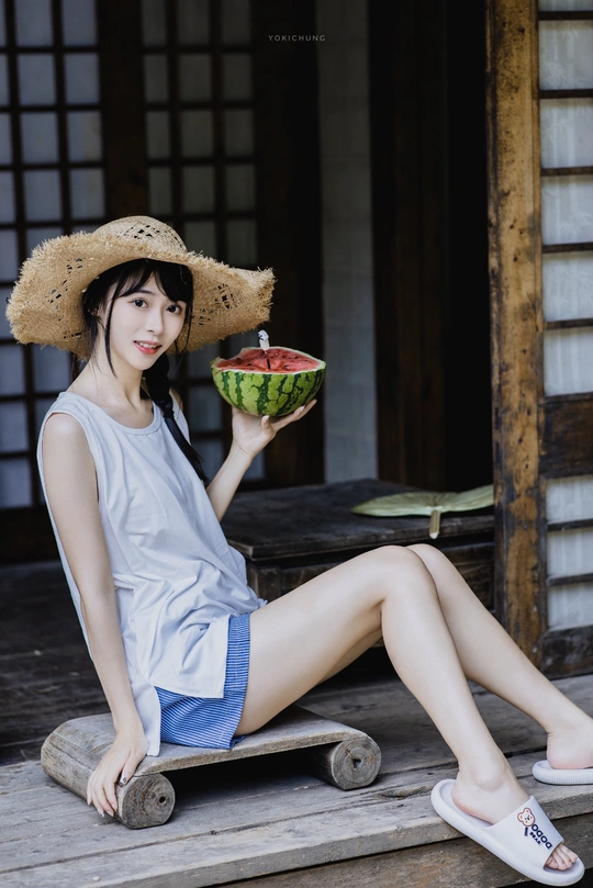 一个戴帽子的小女孩抱着一个西瓜坐在木滑板上