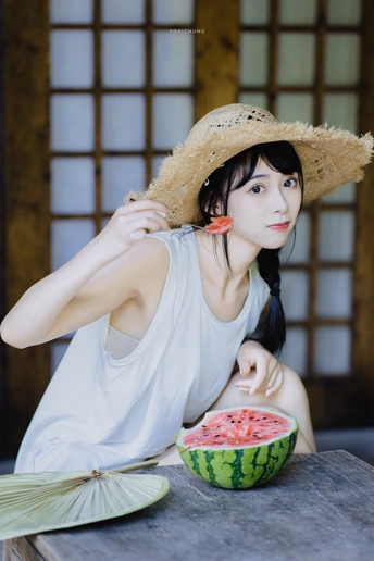 一个戴帽子坐在桌子旁吃西瓜的年轻女子
