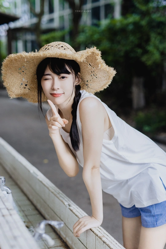 一位年轻女子戴着草编帽子倚靠在围墙上