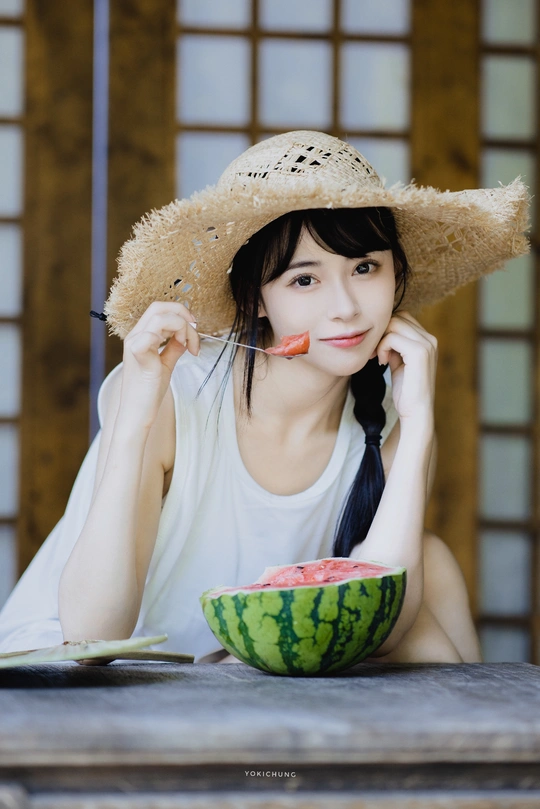 一个戴草帽的年轻女子坐在桌子旁 手里拿着一碗西瓜。