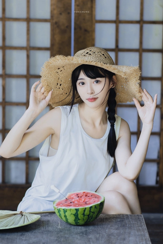 一个戴草帽的年轻女子坐在桌子旁 手里拿着一颗西瓜。