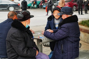 一个老人和女人在一个繁忙的街道上的一张桌子上玩纸牌。