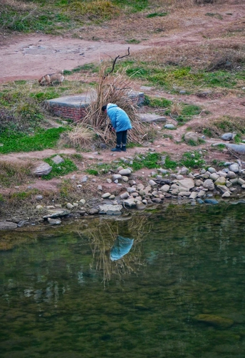一个小男孩站在一块岩石上 向下看着流入湖或溪流的小片水域。