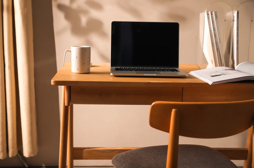 一个小房间里 一个打开的笔记本电脑坐在一个小木桌子上 桌子前面是一个窗户。