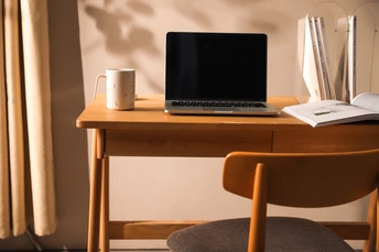 一个小房间里 一个打开的笔记本电脑坐在一个小木桌子上 桌子前面是一个窗户。