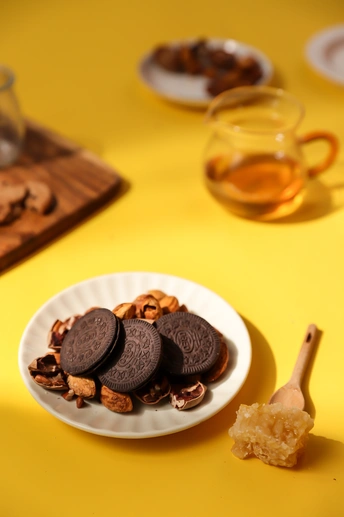 一个带有饼干和杏仁的白盘子放在一个黄色的桌子旁边 旁边放着一杯茶和一小杯茶。