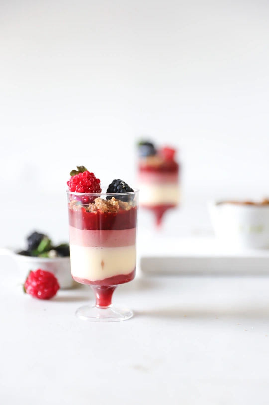 一个带有小白盘的白桌子上放着食物 其中包括一份草莓、奶油和酸奶的甜点。