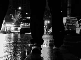 一个人站在雨夜湿漉漉的人行道上 手中拿着一把伞。