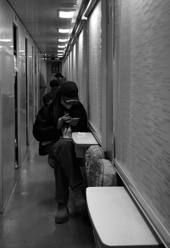 一个人坐在火车走廊的长椅上 正在看手机。