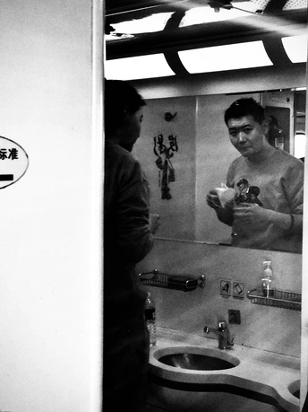 一张黑白照片 一个男子站在浴室里 正在镜子前刷牙。